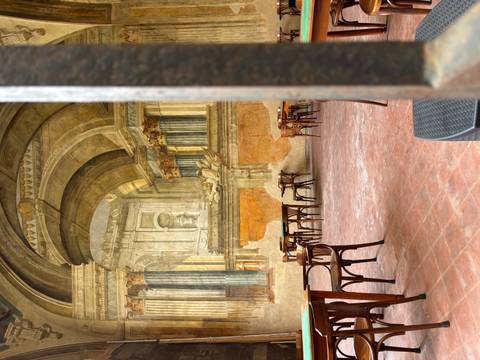       Atmospheric cafe courtyard with empty wooden tables set against grand frescoed Renaissance arches
  