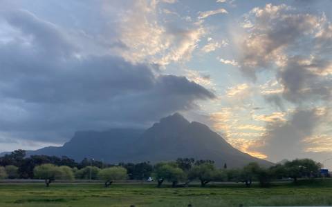       Silhouetted mountain peak at dawn with dramatic clouds and pastel sky.
  