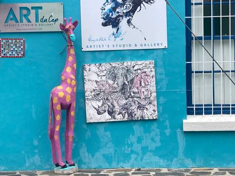       Colorful turquoise wall with modern African art, a pink spotted giraffe sculpture and a gallery sign in Bo-Kaap
  