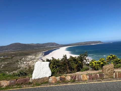       Sweeping view of a long white sand beach curving between turquoise sea and green hills on a clear day
  