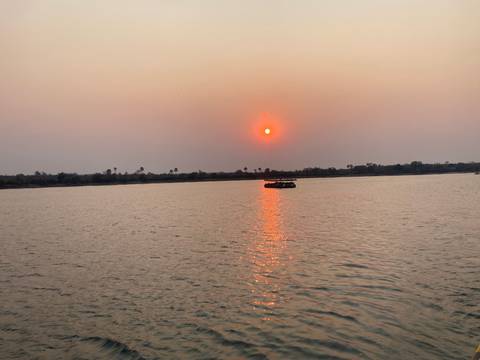       Fiery red sun setting over a wide river with a small cruise boat reflecting on the water
  