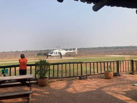       Tourist waiting near a white helicopter on a helipad overlooking dry bushland
  
