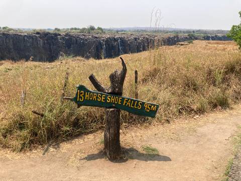       Wooden trail sign reading 'Horse Shoe Falls 45m' with Victoria Falls gorge in the background
  