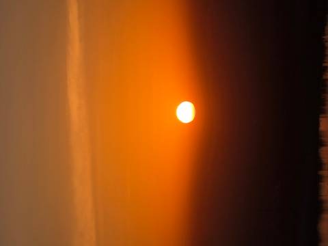       Brilliant orange sun setting over a hazy horizon.
  