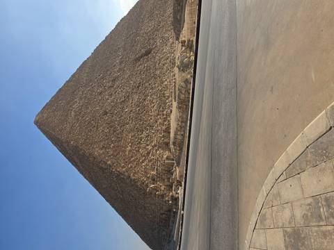       Close-up shot of a massive pyramid rising steeply beside a paved road under a clear blue sky.
  
