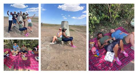       Picnic scenes on red Maasai blankets with travellers relaxing and posing beside a stone border marker.
  