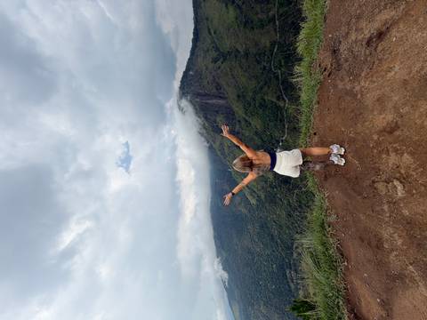       Woman with open arms looks over misty green mountains and valleys under dramatic clouds
  