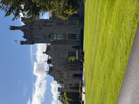       Grand stone castle hotel with manicured lawn flying the Irish flag on a sunny day
  