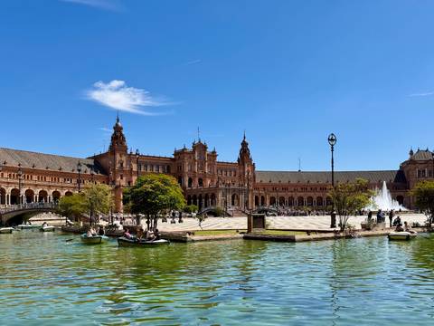       Plaza de España in Seville with rowboats on the canal and ornate towers under blue sky
  