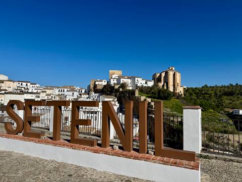       Large metal letters spelling SETENIL with white hill town and castle in the background
  