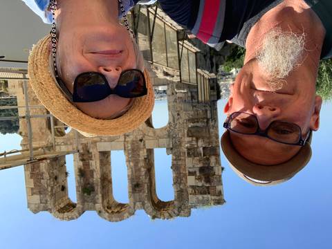       Selfie of two travelers with Odeon of Herodes Atticus ruins behind on the Acropolis
  