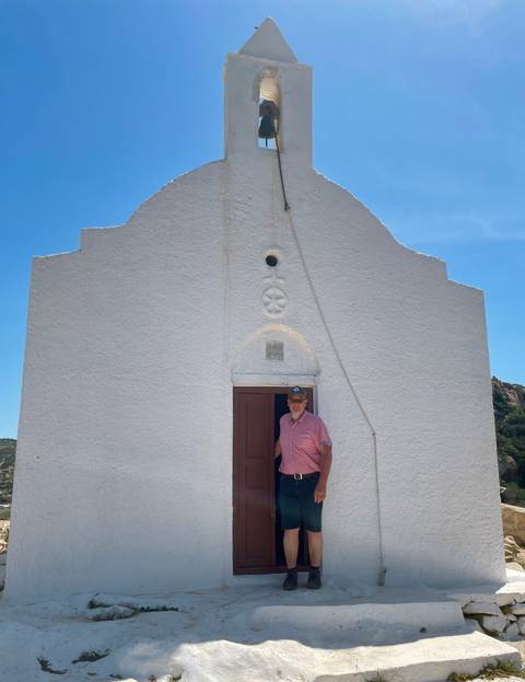       Man standing in front of a small white countryside chapel under bright sky
  