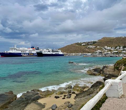       Two large ferries anchored in turquoise harbor waters with hillside village beyond
  