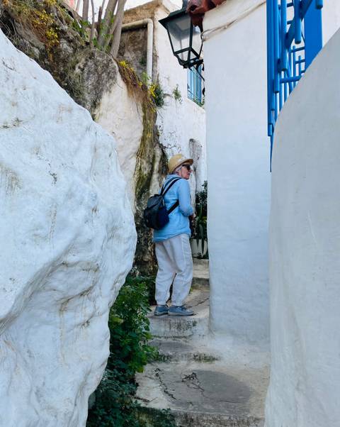       Woman with backpack and straw hat walking through narrow whitewashed alley
  