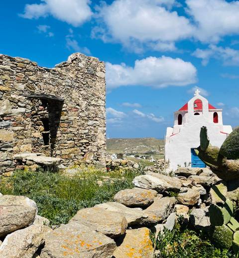       Rugged stone ruin beside small white and red chapel overlooking rural Mykonos landscape
  