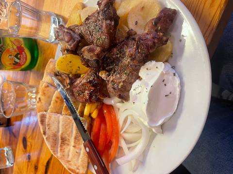       Close-up of a hearty Greek plate featuring grilled lamb, pita bread, vegetables and yogurt on a restaurant table.
  
