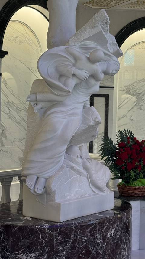       Indoor white marble sculpture of angelic figure with bouquet of red roses beside
  