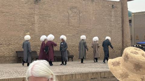       Men in traditional striped robes and large wool hats walking along mud-brick wall in Khiva
  