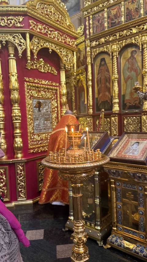      Close-up of lit prayer candles in an ornate gold stand before richly decorated icons.
  