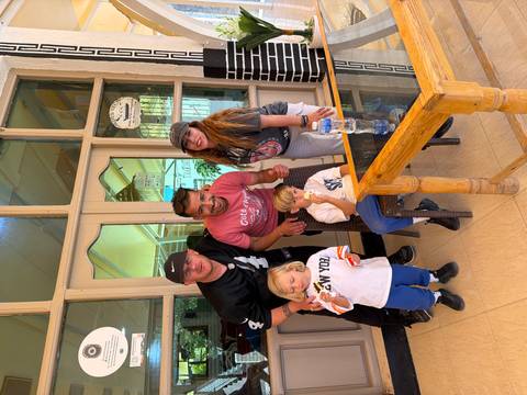       Two adults, a guide and two small children smiling together inside a café entrance
  