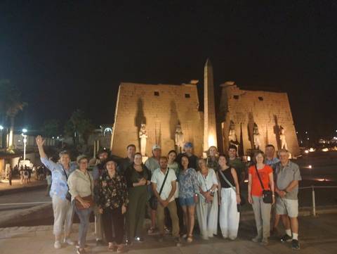       Tour group poses at night before the illuminated statues and pylon of Luxor Temple.
  