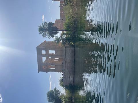       Island kiosk of Philae Temple rising from placid water under a bright midday sunbeam.
  