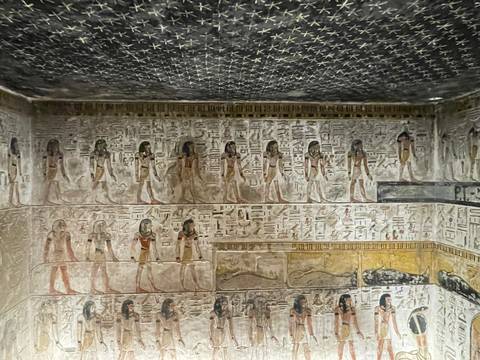       Interior tomb chamber richly painted with rows of Egyptian figures and starry ceiling detail.
  