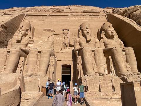       Massive seated statues of Abu Simbel dwarf visitors gathered at the monument’s entrance.
  