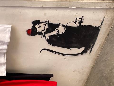       Stencil graffiti of a fez-wearing rat holding cheese on a white wall.
  