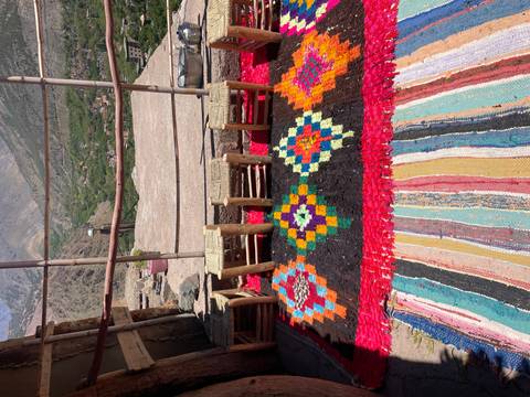      Colourful woven rugs and low stools arranged on a terrace overlooking a lush mountain valley.
  