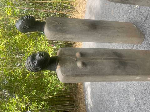       Two weathered stone statues of abstract human forms stand on a gravel path within a bamboo grove.
  