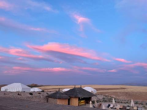       Pink-tinged sunset clouds stretch above cream canvas tents set on a rolling desert plain.
  
