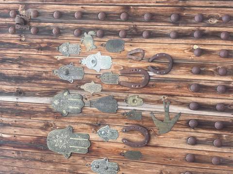       Weathered wooden door adorned with metal hamsa hand amulets, horseshoes and other talismans.
  