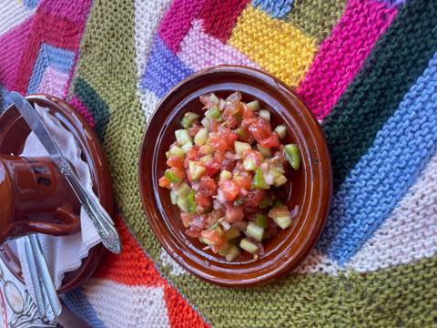       Fresh chopped tomato and cucumber salsa served in a brown clay dish atop a colorful woven cloth.
  