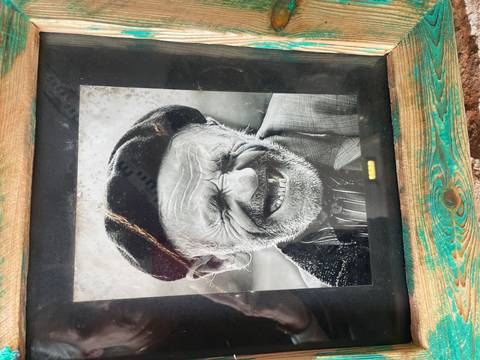       Framed black-and-white portrait of an elderly man laughing, displayed against rustic wood.
  