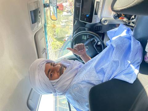       Friendly driver in traditional white turban and robe smiles and gives a thumbs-up from the front seat.
  