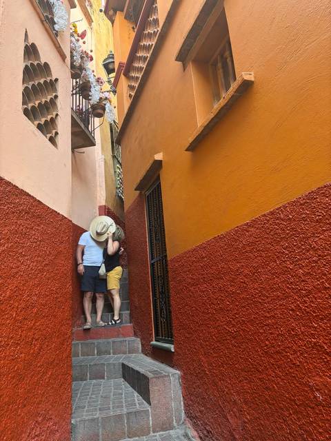       Couple sharing a kiss in a narrow brightly painted alleyway with red and orange walls
  