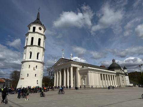       Vilnius Cathedral and tall bell tower dominate a bustling city square under streaked clouds.
  