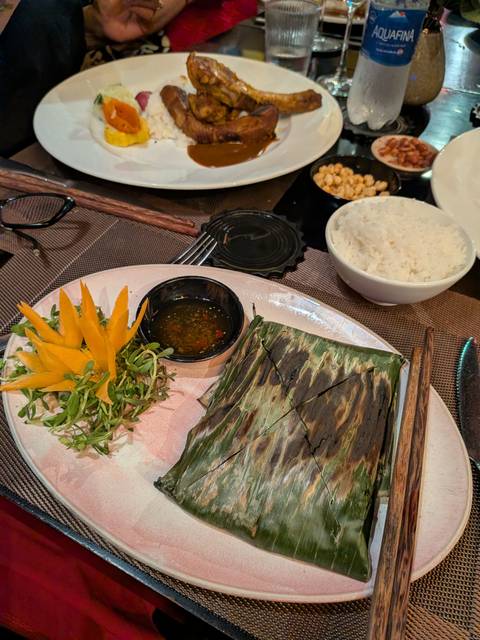       Plated Vietnamese dish wrapped in banana leaf with dipping sauce and carved garnish.
  