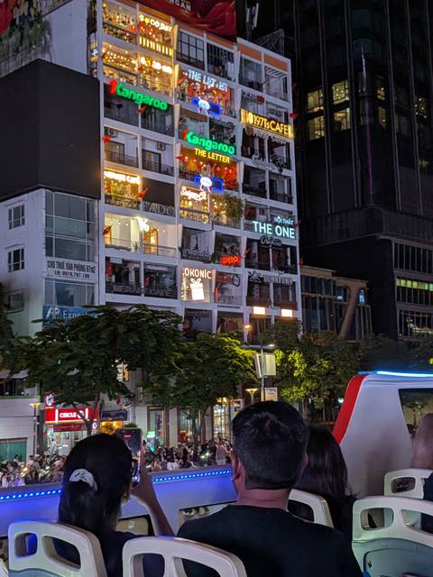       Night view of neon-lit apartment building cafés along Nguyen Hue in Ho Chi Minh City.
  