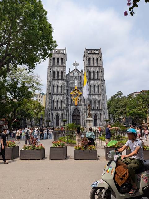       Gothic St. Joseph's Cathedral in Hanoi towers over bustling visitors and street vendors.
  