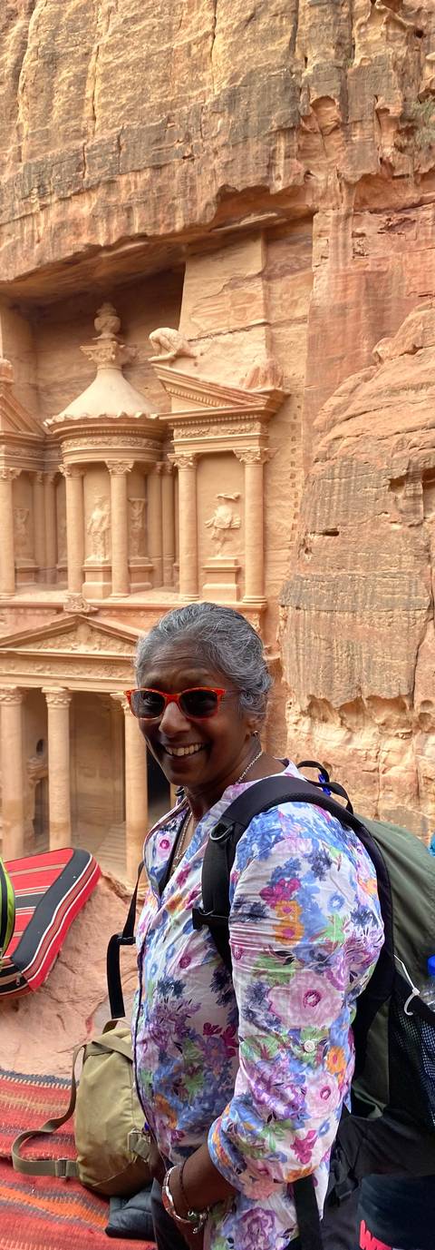       Smiling traveler with the carved façade of Petra's Treasury looming behind.
  