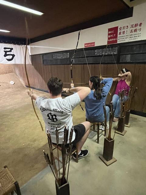       Indoor archery class where participants draw traditional bows in a wood-panelled range
  
