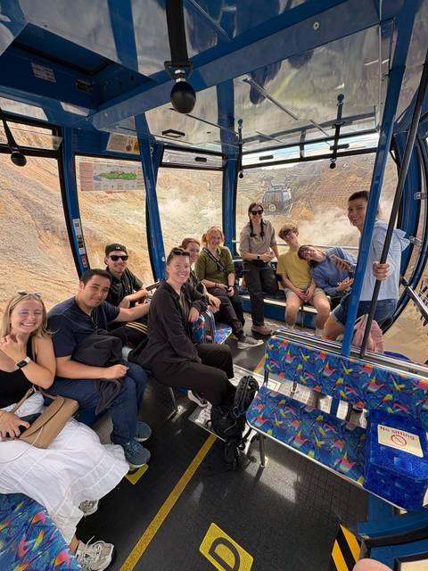       Smiling tour group seated inside a glass gondola overlooking volcanic terrain
  