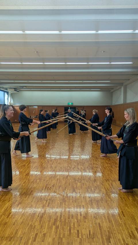       Participants in traditional kendo uniforms practice sword forms in a polished wooden hall
  