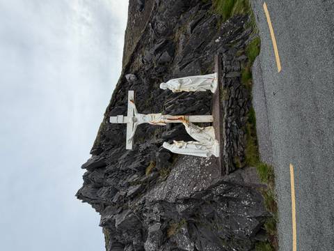      A roadside crucifixion scene with three white statues set against dark jagged rocks.
  
