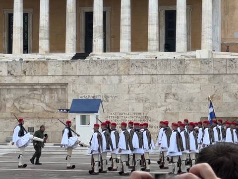       Evzone guards in traditional white uniforms and red caps march in formation during the changing of the guard ceremony.
  