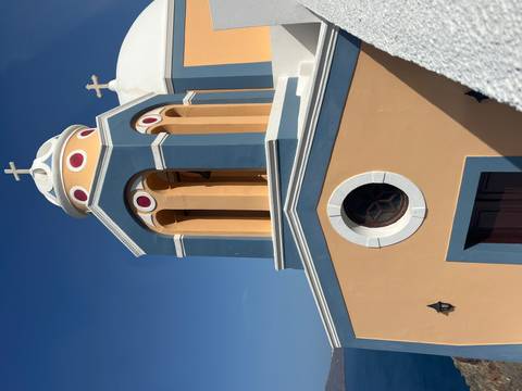       Close view of a pastel orange and blue bell tower with rounded arches and small crosses under clear sky.
  
