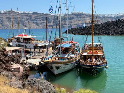       Wooden excursion boats packed with passengers are moored beside volcanic cliffs in the Santorini caldera.
  