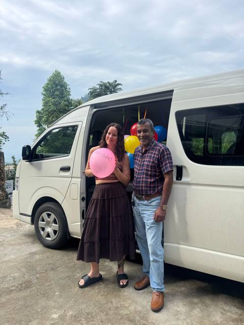       Traveller with birthday balloon poses beside a van decorated with colourful balloons.
  